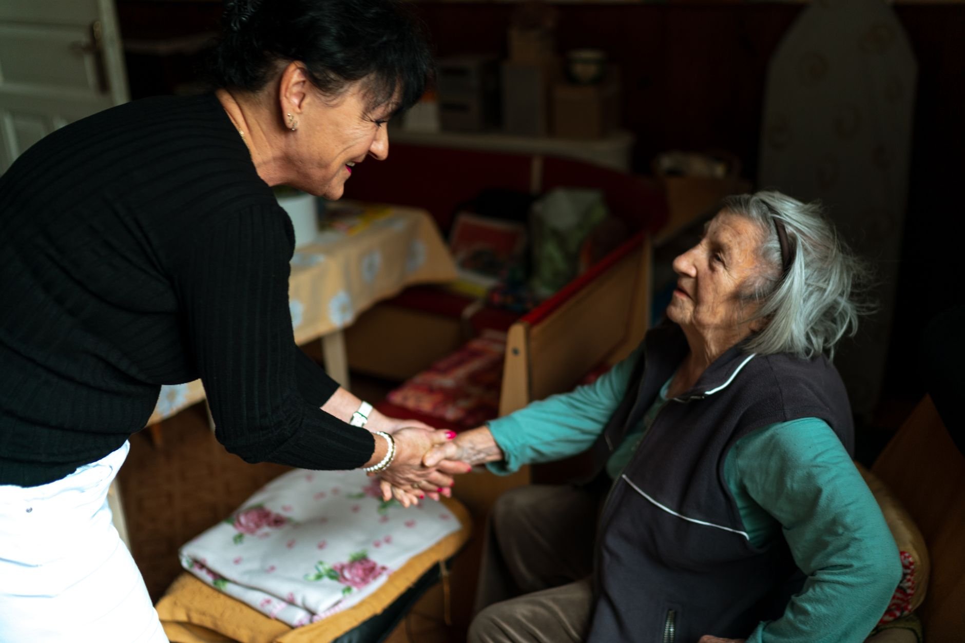 An elderly caregiver warmly greeting a senior woman at home