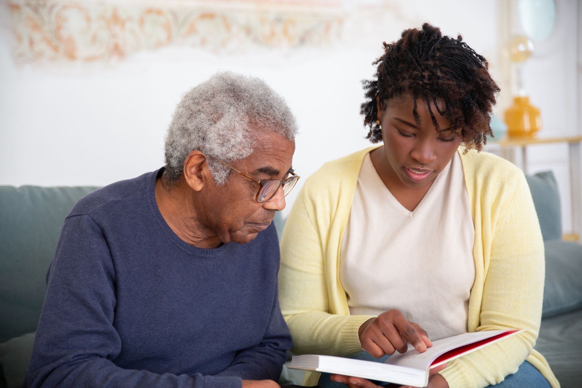 A caregiver helps a senior man with reading, providing attentive support at home.
